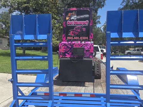 904Tree stump grinder loaded on trailer — rear view between blue ramps with Got Stumps? branding
